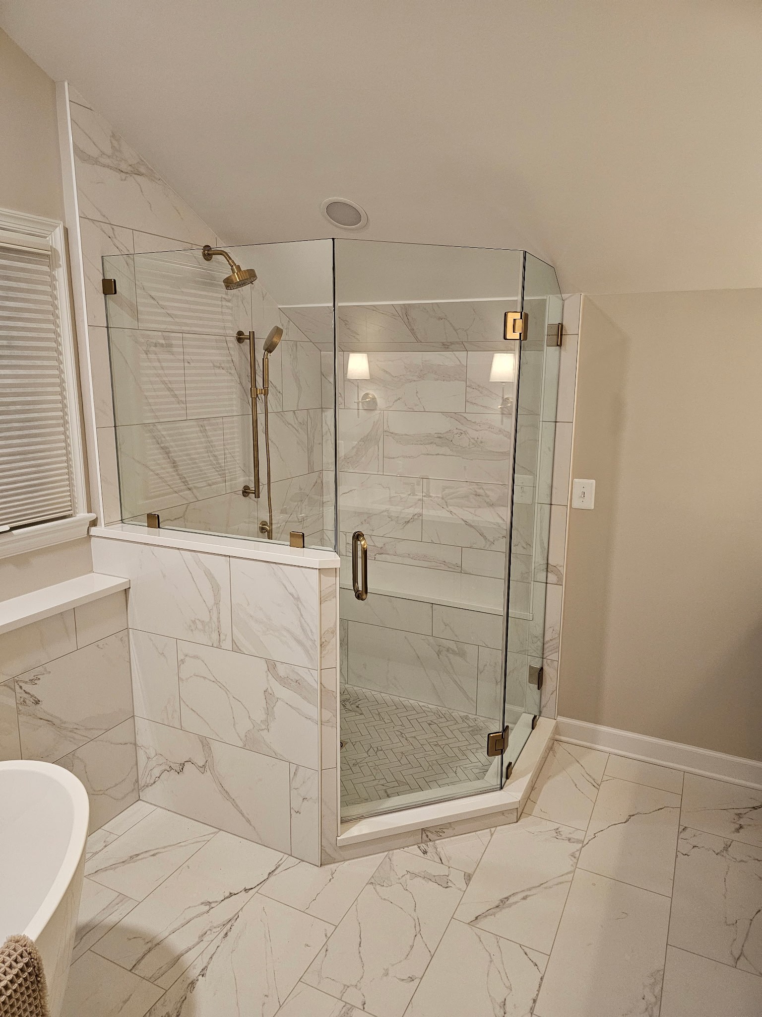 Custom frameless shower enclosure with gold-tone hinges and handles beside a bathtub.