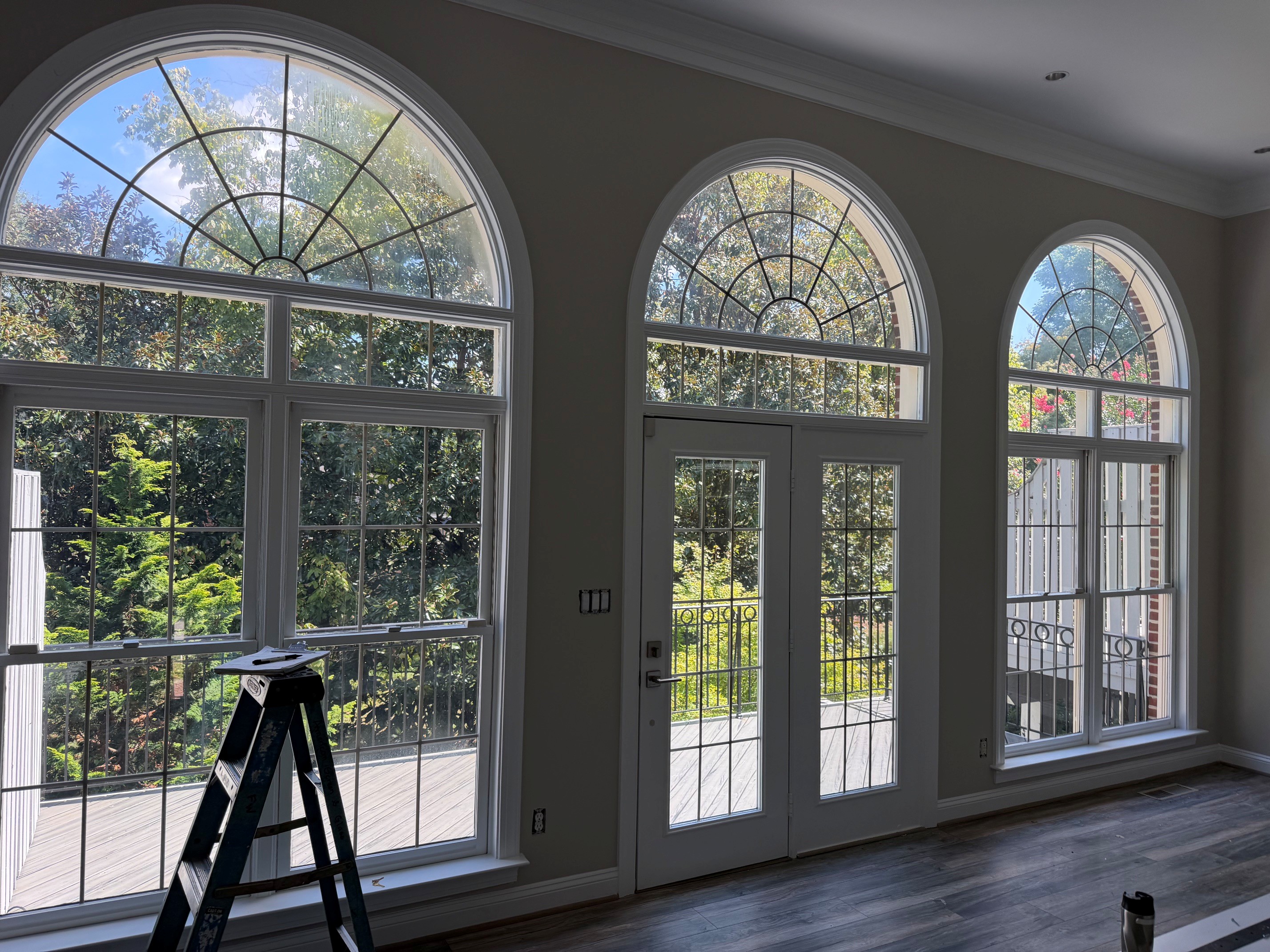 Tall arched windows and glass French doors overlooking a leafy garden.